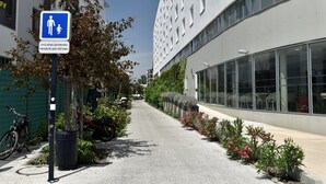 Un bâtiment moderne doté d’une promenade piétonne, d’un panneau indiquant la priorité aux cyclistes autorisés, et d’un vélo garé près du bâtiment.