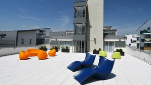 Une terrasse sur le toit, dotée de mobilier contemporain, d’un ascenseur à parois vitrées et offrant une vue sur les bâtiments environnants.