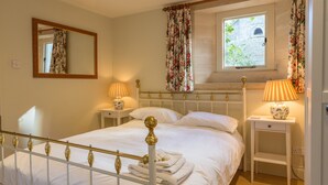 Un lit bien fait, avec du linge de lit blanc, une table de chevet avec une lampe et une fenêtre ornée de rideaux à motifs floraux.