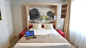 Ein Hotelzimmer mit Bett, Laptop, großem gerahmten Bild an der Wand und einem fenster mit Vorhängen.