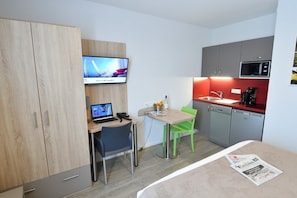 A compact hotel room with a desk, a laptop, a television, a small kitchenette, and a bed with a newspaper. - Studio centre historique Bordeaux | Climatisation (Bordeaux)