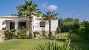 Une villa blanche à la façade en pierre, bordée de palmiers et dotée d’une pelouse bien entretenue.