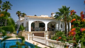 Une villa blanche avec une piscine, entourée de palmiers et d’une clôture blanche.