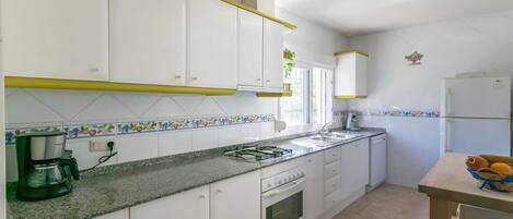 A kitchen with white cabinets, a gas stove, a coffee maker, and a refrigerator.