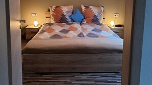 Quarto com cama, duas mesas de cabeceira com luminárias, ventilador de teto e um quadro na parede.