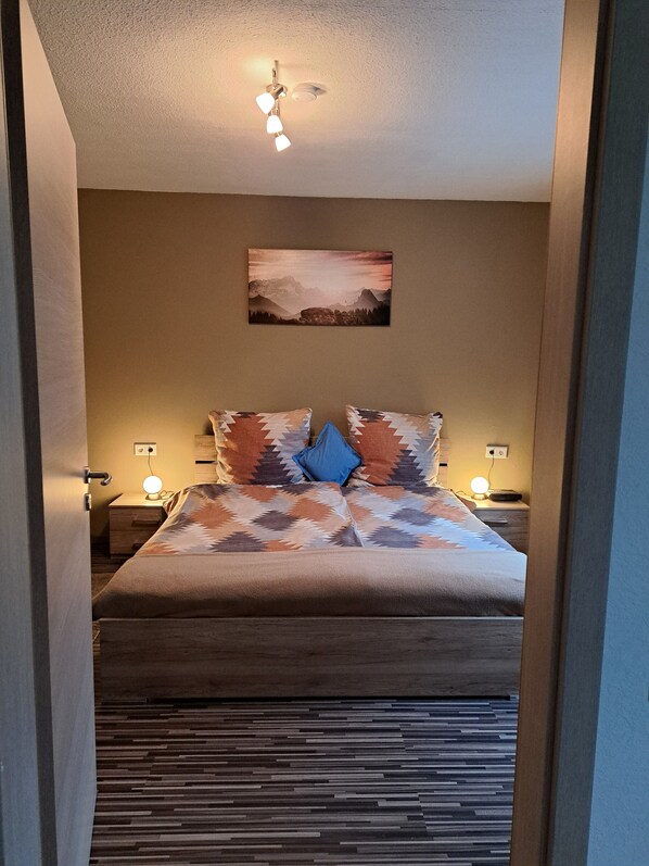 A bedroom with a bed, two bedside tables with lamps, a ceiling fan, and a wall-mounted painting. - Ochmann's apartment in the beautiful Sauerland (Remblinghausen)