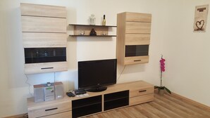 Uma sala de estar moderna com televisão de tela plana, armários de madeira e uma pequena estante com objetos decorativos.