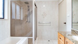 A modern bathroom with a glass-enclosed shower, a glass door, a vanity with a granite countertop, and a white bathtub. - Hill Top Water and Bush Views (Sussex Inlet)