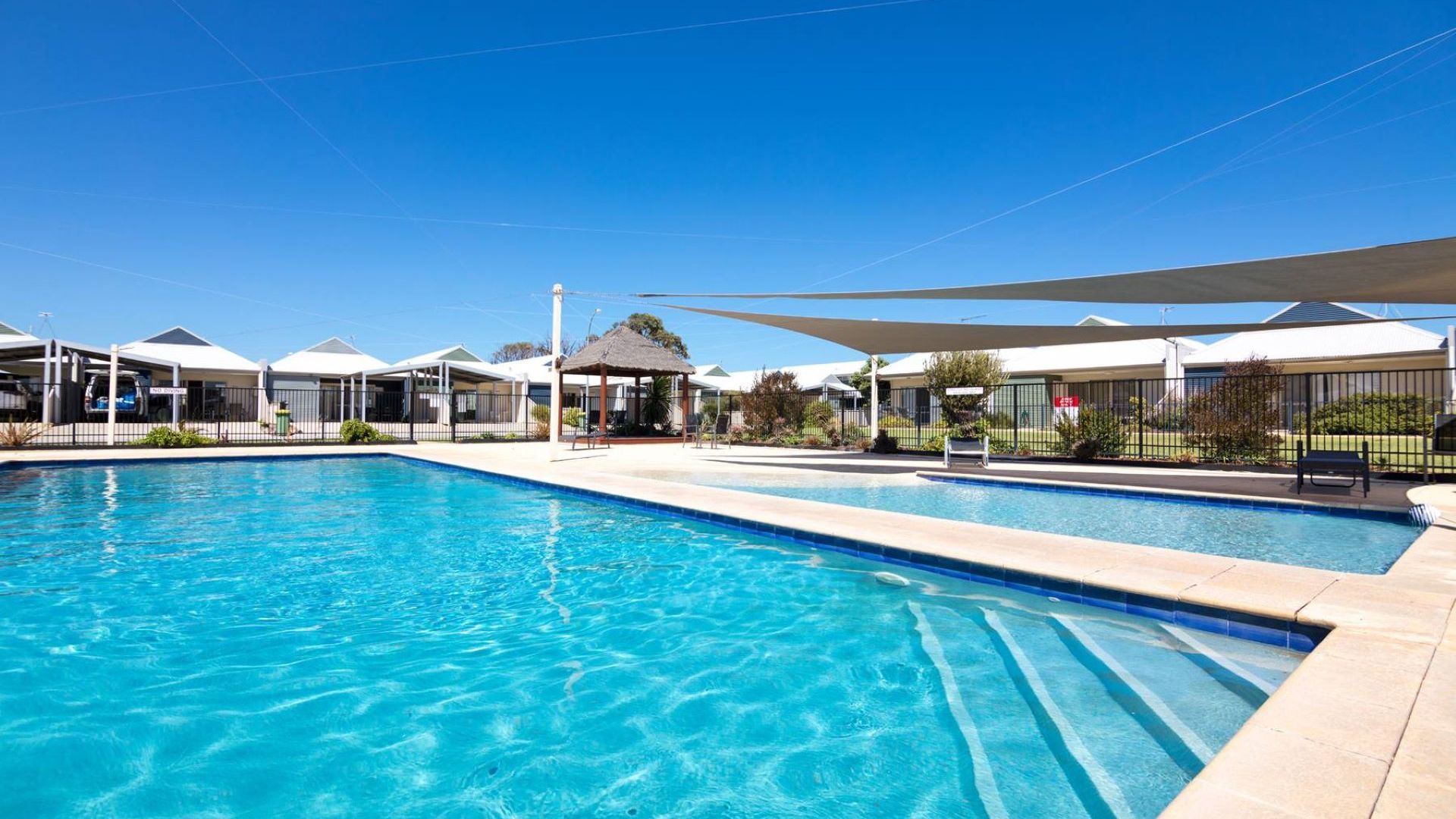 A swimming pool with a clear blue water surface, surrounded by covered seating areas and a gazebo.
