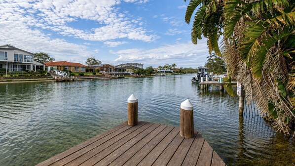 A wooden dock extending into a calm body of water with houses and a boat docked on the opposite side.