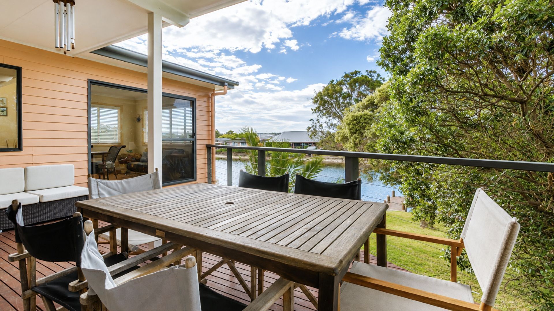 A wooden deck with a table and chairs, overlooking a body of water and greenery.