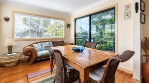 A dining area with a wooden table, wicker chairs, a cushioned bench, and a large window with blinds.