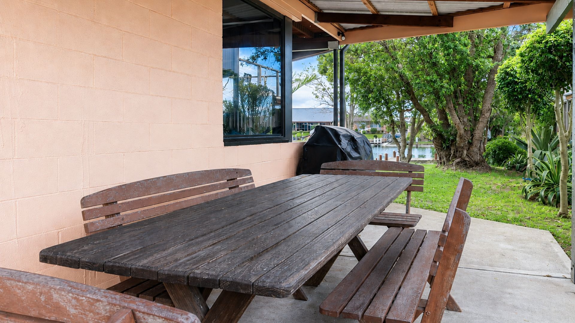 Un patio al aire libre con mesa y bancos de madera, una parrilla y vistas a un cuerpo de agua y vegetación.