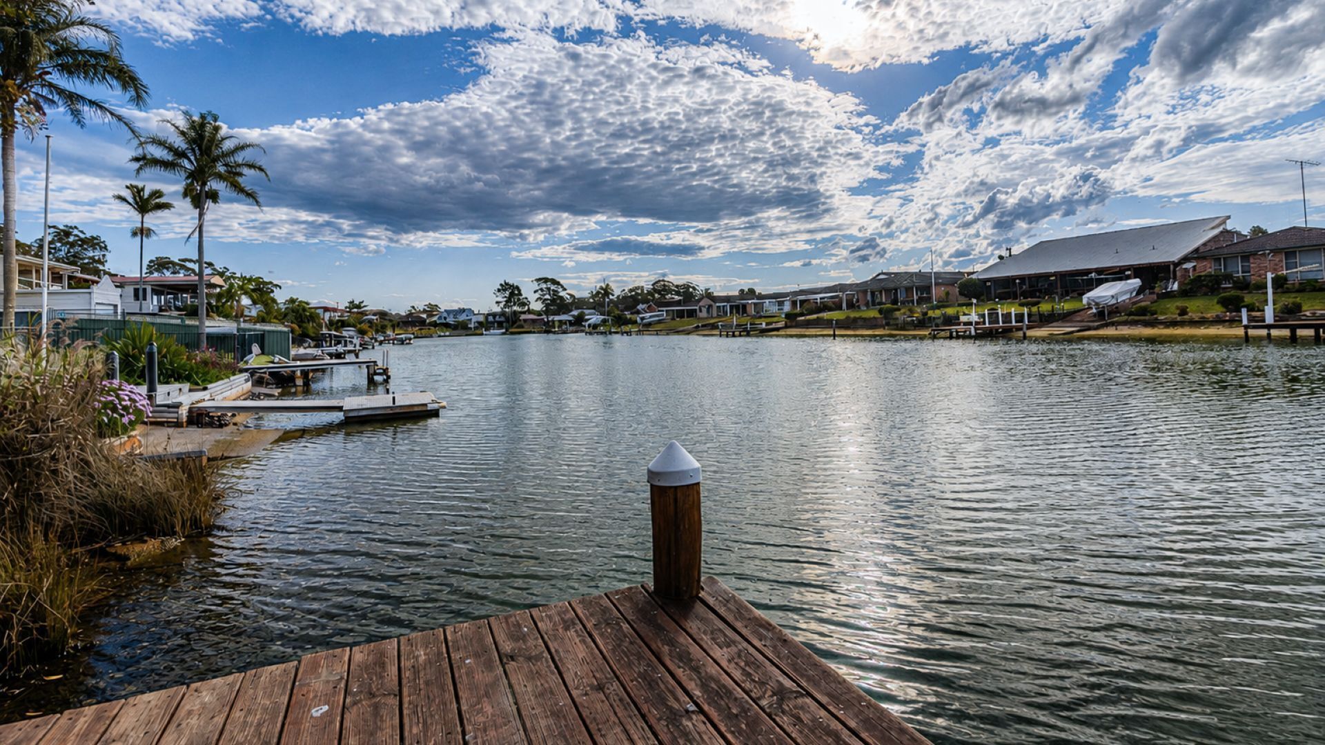 A waterfront property with a dock, a boat, and a row of houses in the background.