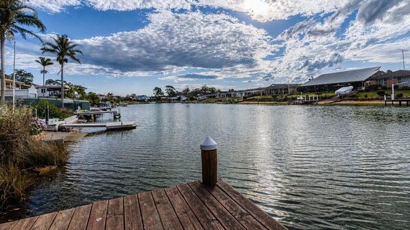 A waterfront property with a dock, a boat, and a row of houses in the background. - Waterfront Delight on Cater (Sussex Inlet)