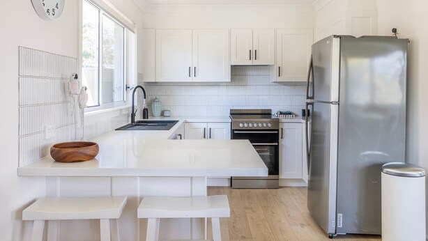 Una cocina moderna con muebles blancos, un refrigerador de acero inoxidable, horno empotrado y una isla grande con un bol y taburetes.