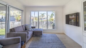 Una sala de estar moderna con un sofá seccional gris, un televisor de pantalla plana montado en la pared y un ventanal con vistas al jardín.