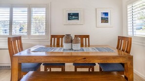 Un comedor con una mesa de madera, sillas con cojines azules, un mantel tejido y dos jarrones decorativos.