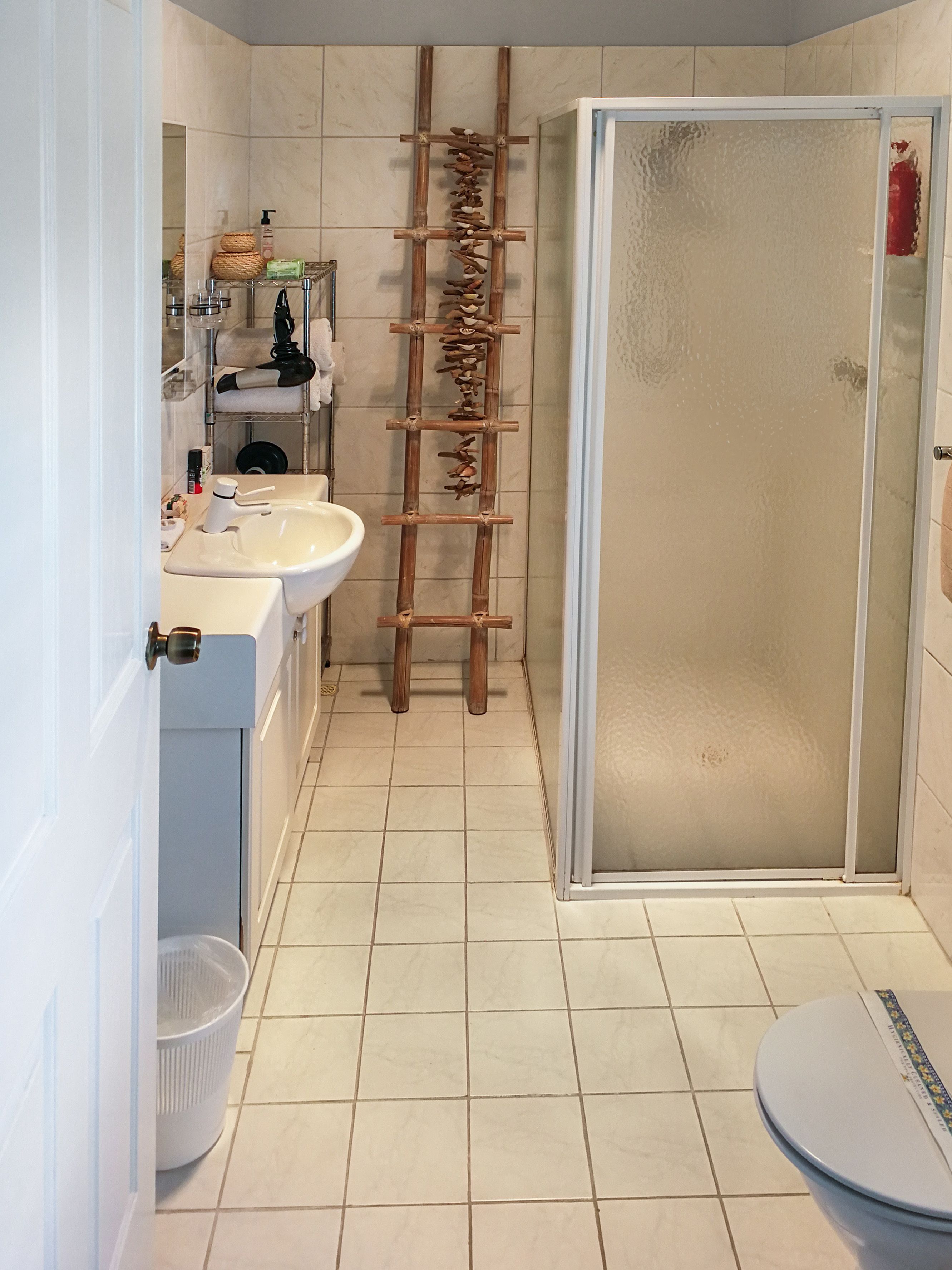 A bathroom with a white sink, a mirror, a shower enclosure, and a wooden ladder.