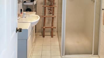 A bathroom with a white sink, a mirror, a shower enclosure, and a wooden ladder.