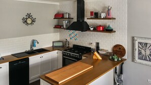 A modern kitchen with white cabinetry, a wooden countertop, a built-in stove, and a black range hood. There are shelves above the stove holding various kitchen items. - Airport B&B (Redcliffe)