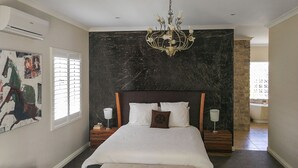 A bedroom with a large bed, a chandelier, a marble wall, and a painting on the wall. - Airport B&B (Redcliffe)