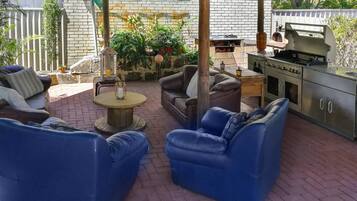 Un patio al aire libre con asientos acolchados azules, una mesa redonda y una parrilla.
