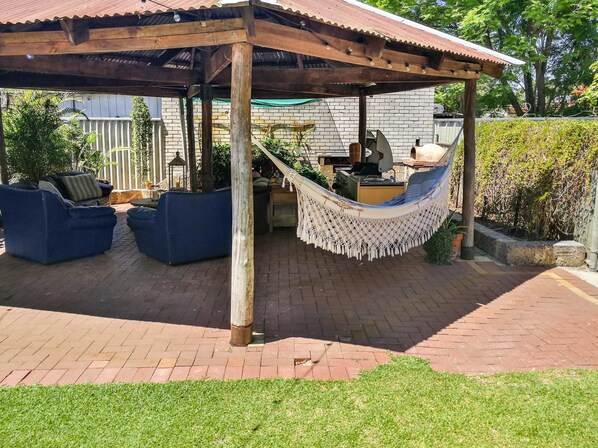 Un patio techado con una hamaca, sofás azules y una zona de barbacoa.