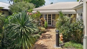 A well-maintained garden with a variety of plants and a paved pathway leading to a building with a corrugated metal roof. - Airport B&B (Redcliffe)