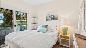 Une chambre avec un grand lit, une table de chevet avec une lampe, un tableau au mur et une vue à travers une porte coulissante.