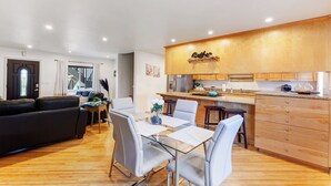 A modern kitchen with wooden cabinets, a dining area with a glass table, and a living room with a black sofa. - Point Loma 3 bedroom/2bath (San Diego)