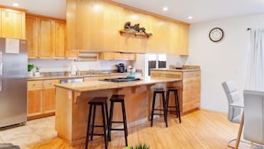 A modern kitchen with wooden cabinets, a central island with stools, a built-in oven, and a clock on the wall. - Point Loma 3 bedroom/2bath (San Diego)