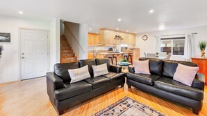 A spacious living area with a black leather sofa set, a wooden floor, and a kitchen in the background. - Point Loma 3 bedroom/2bath (San Diego)