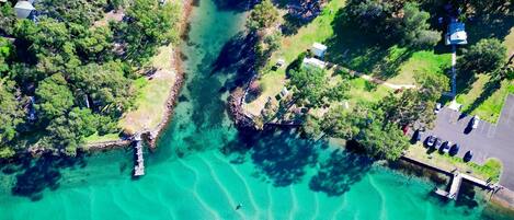 An aerial view of a coastal area with clear turquoise waters, a dock, and a parking area with cars.