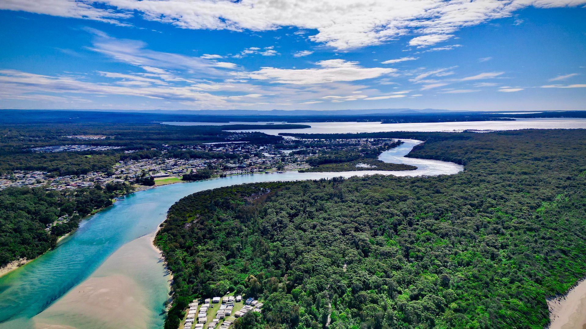 An aerial view of a coastal town with a river, dense forest, and beach.