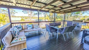 A covered outdoor deck with a barbecue grill, seating area with cushions, and a view of the surrounding landscape. - The Perfect Holiday Home (Sussex Inlet)