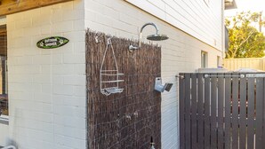 A white brick wall with a bamboo fence, a metal gate, and a sign that reads "OUTDOOR SHOWER". - The Perfect Holiday Home (Sussex Inlet)
