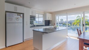 A modern kitchen with a central island, white cabinetry, and a view of a pool and palm trees. - Unbeatable Waterfront Location (Sussex Inlet)