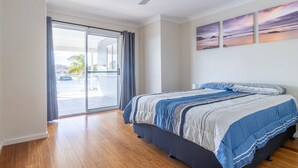 A bedroom with a bed, a sliding glass door leading to a balcony, and two paintings on the wall. - Unbeatable Waterfront Location (Sussex Inlet)