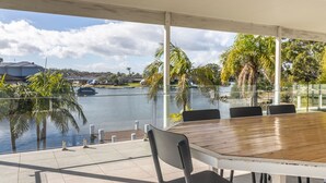 A covered outdoor dining area with a view of a lake and palm trees. - Unbeatable Waterfront Location (Sussex Inlet)