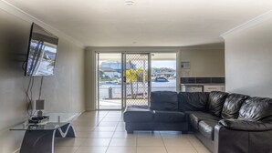 A modern living room with a leather sofa, a flat-screen TV mounted on the wall, and a glass coffee table. - Unbeatable Waterfront Location (Sussex Inlet)