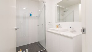 Un bany modern amb plat de dutxa de vidre, un lavabo blanc i un mirall gran.