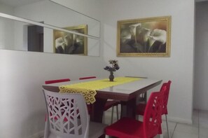 A dining area with a wooden table, red chairs, a yellow tablecloth, and a vase with flowers. There are two framed pictures on the wall.