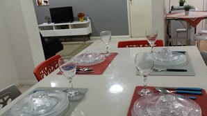 Un comedor con una mesa blanca preparada para cuatro personas, incluyendo platos, vasos y cubiertos.