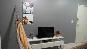 Una sala de estar con una hamaca, un televisor sobre un soporte blanco y una puerta.