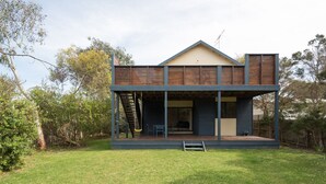 A modern two-story house with a balcony, a covered outdoor seating area, and a staircase leading to the upper level.