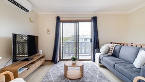 A living room with a flat-screen TV, a gray sofa, a wooden coffee table, and a sliding glass door leading to a balcony. - Perfect family holiday (Berrara)