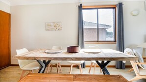 A dining area with a wooden table, white chairs, and a view of a brick building through a window. - Perfect family holiday (Berrara)