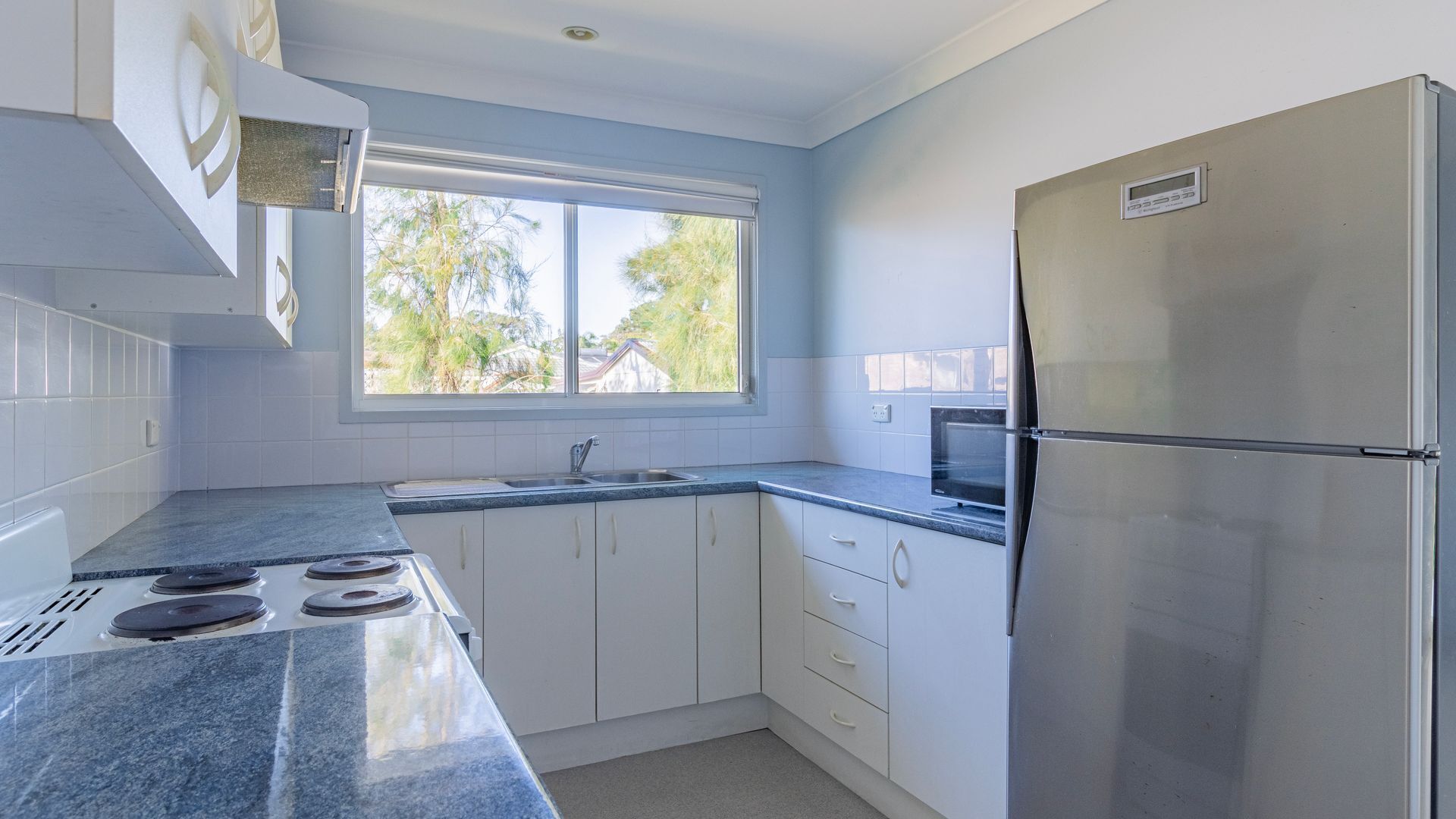 Une cuisine moderne avec des meubles blancs, un réfrigérateur en acier inoxydable, un four à micro-ondes et une cuisinière à gaz.