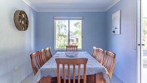 Ein Esszimmer mit einem für sechs Personen gedeckten Tisch, einem Fenster mit Blick ins Grüne und einem an der Wand befestigten Regal.